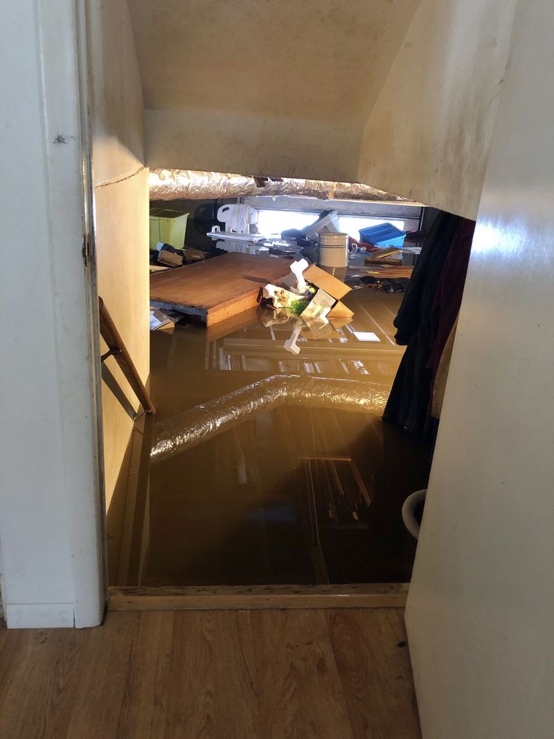 A basement flooded with standing water up to the floorboards, belongings floating